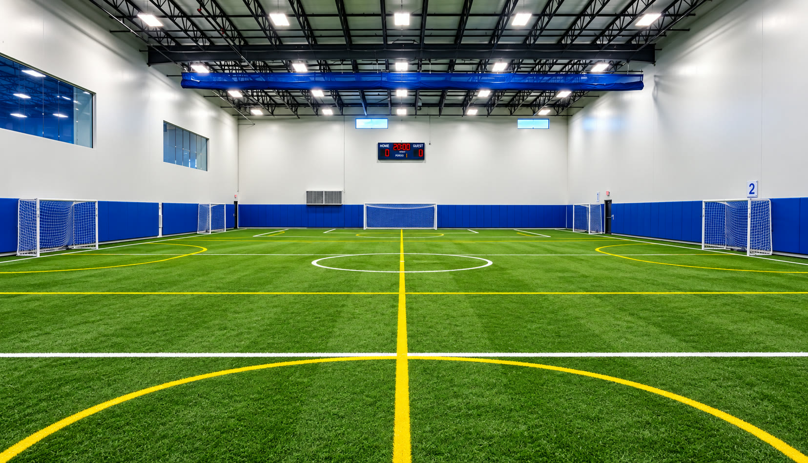 Indoor turf field with scoreboard and blue wall padding at Cadence Sports Center in Joliet